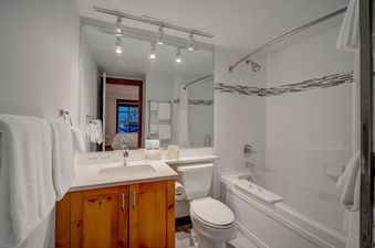 The bathroom features a modern vanity with a large mirror, track lighting, a toilet, and a bathtub with a shower.