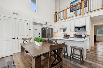 An open-concept kitchen and dining area in Quarry B10, featuring a wooden dining table, white kitchen cabinets, stainless steel appliances, and an internal balcony overlooking the space.