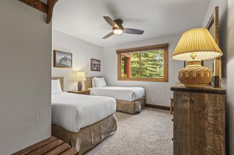 A cozy guest bedroom at Snow Flower 56 Park City with two twin beds, rustic furnishings, and a large window offering a view of evergreen trees.