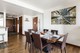 A modern dining room with a wooden table, brown leather chairs, and a large nature-inspired artwork.