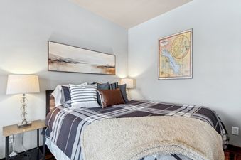 A cozy king bedroom in Cana Loft 203 with a striped plaid comforter, a glass lamp, and an abstract landscape painting above the bed.