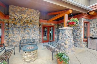 A stone patio with a stone fire pit, two wrought iron benches, and a potted plant