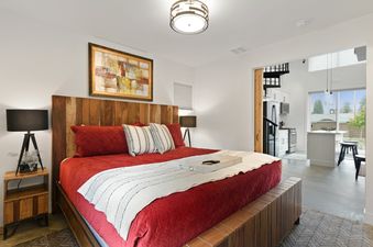 The king-size bed in Quarry A7's bedroom, featuring a red quilted duvet and rustic wooden furniture, with the living area and kitchen visible beyond.