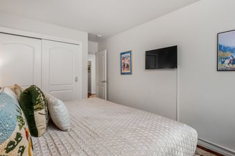 A cozy bedroom with a bed adorned with colorful pillows, closet doors, and a mounted television.