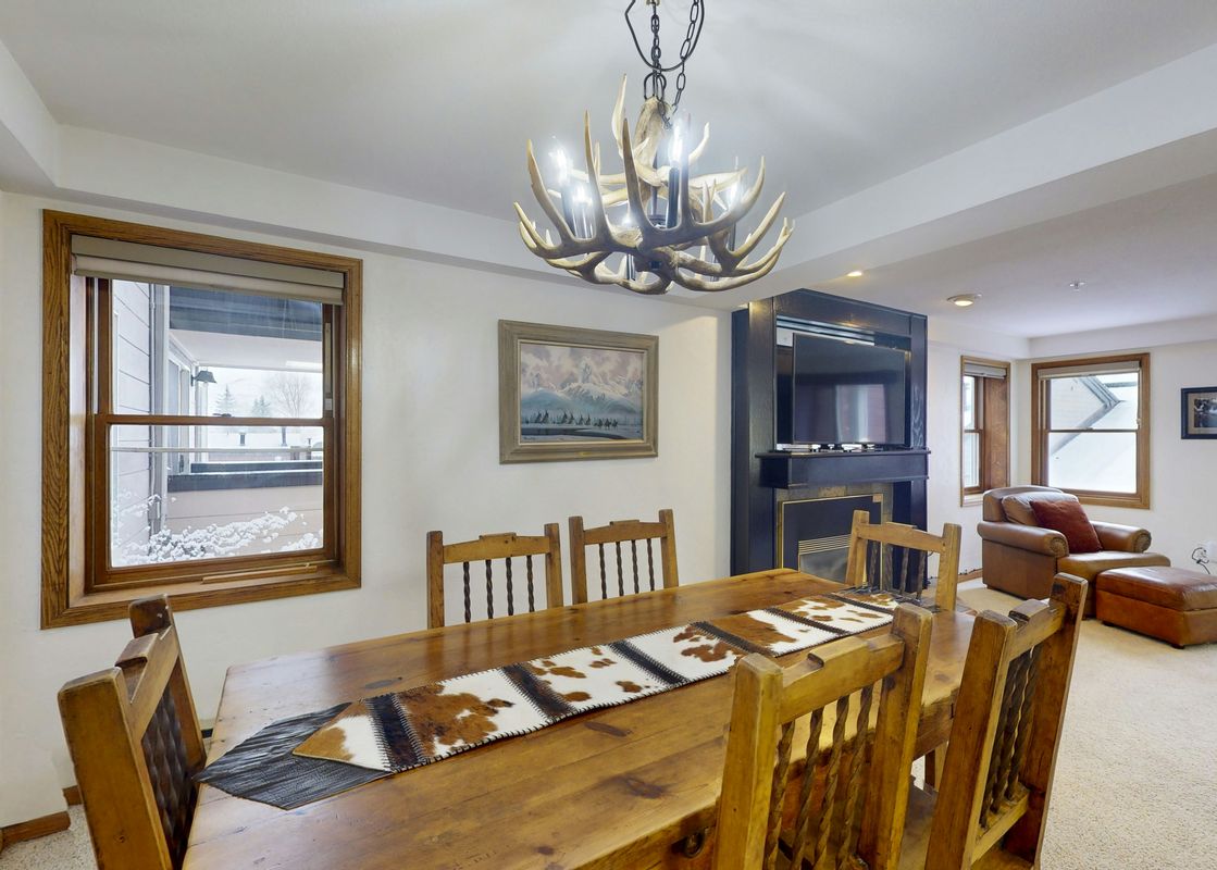 The dining room and living room are elegantly furnished with a wooden dining table, antler chandelier, and a cozy armchair, offering a rustic yet sophisticated ambiance.
