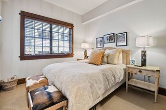 A cozy bedroom with a queen bed, decorative pillows, cowhide ottomans, and two bedside lamps.