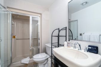 A white bathroom with a tiled shower, a toilet, and a sink with a towel that says 'fresh.'