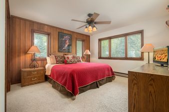 Cozy bedroom at Teewinot C5 featuring a red quilted bed, wood-paneled walls, and large windows.