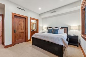 The bedroom at Blue Bird Vista at Hummingbird Lodge features a large bed with a dark frame, two nightstands with lamps, and wooden doors leading to other areas of the unit.
