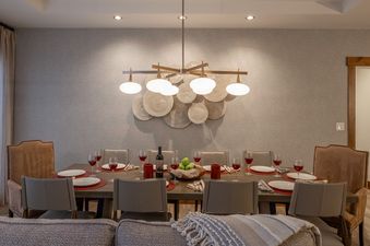 A beautifully set dining table with wine glasses, plates, and a decorative centerpiece, illuminated by a modern chandelier.