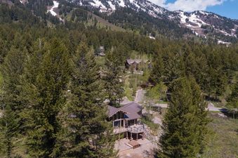 An aerial view of the Fisher House nestled in a lush forest with snow-dusted mountains in the background.