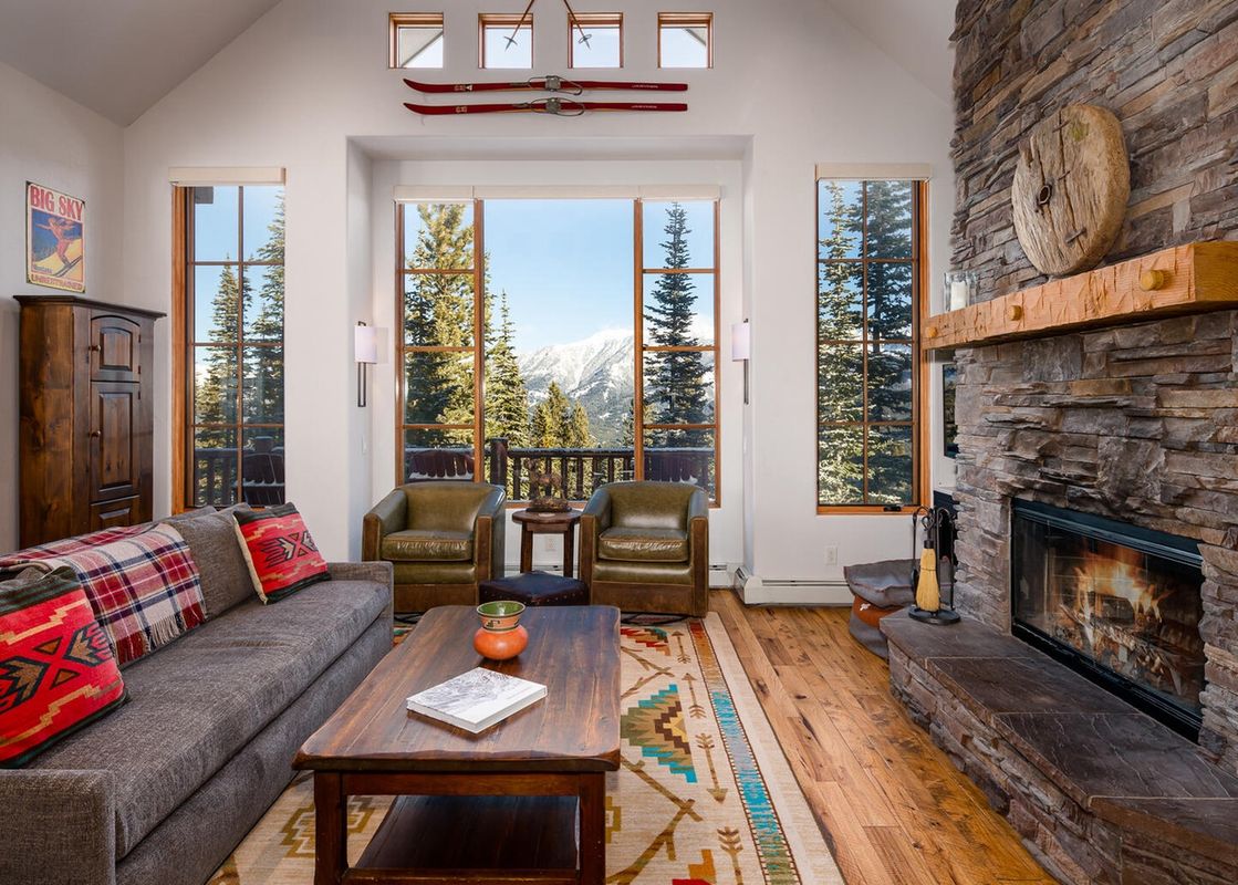 A living room with a fireplace, a large sectional sofa, two leather chairs, and a large window with views of the mountains.
