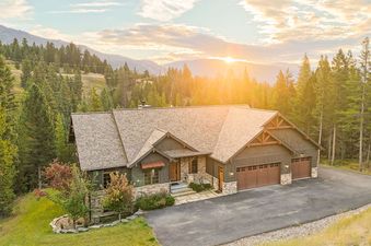 An aerial view of the Antler Ridge 316, a rustic stone and wood home, nestled amidst a dense forest of pine trees, bathed in the warm glow of a sunset.