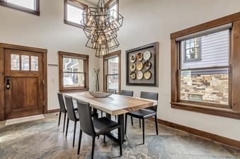 A modern dining area at The Peak at Town Lift features a large wooden table with black chairs, a geometric chandelier, and multiple windows with dark wood frames.