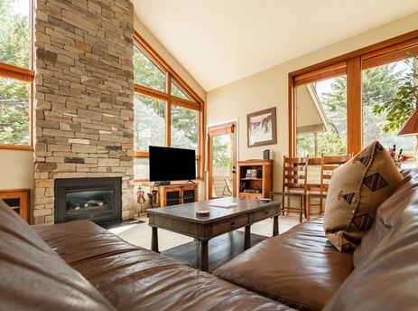 Warm living room at Park City Red Pine Mountain Haus featuring a towering stone fireplace, comfortable leather seating, and large windows with forest views.
