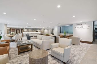 A spacious and modern hotel lounge with comfortable seating areas, a reception desk, and a 'Charter Steakhouse' sign on the wall.