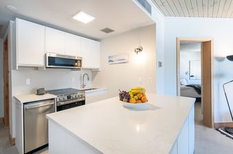 A modern kitchen with stainless steel appliances and white cabinets, with a fruit bowl on the kitchen island.