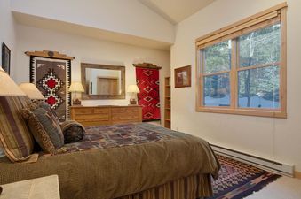 A cozy bedroom in Moose Creek 14 with Southwestern decor, a comfortable bed, wooden furniture, and a large window looking out onto a winter scene.