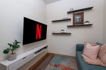 A cozy living area featuring a wall-mounted TV displaying the Netflix logo, a long floating media console, and a teal sofa with decorative pillows.
