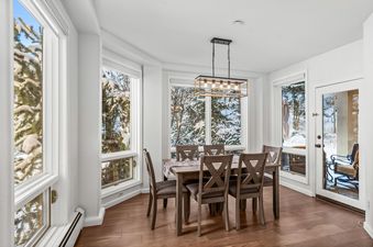 A dining room with a wooden table and chairs set in front of a window with snow-covered trees outside.