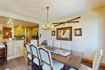 A dining room with a wooden table, chairs, and a chandelier with antlers.