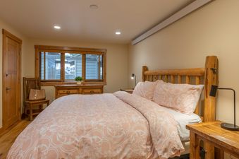 A rustic bedroom in Nez Perce A2 featuring a large bed with pink patterned bedding, log-style wooden headboard, and matching wood furniture.