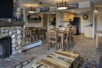 A spacious living area in the Two Bedroom Suite Beaver Run Resort, featuring a stone fireplace, a flat-screen TV, a rustic wooden dining table, and a well-equipped kitchen with light wooden cabinets and modern appliances.