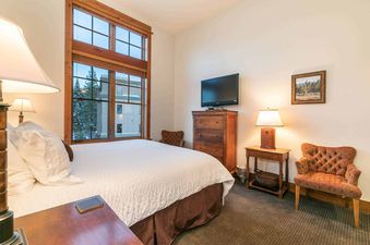 A bedroom with a king-sized bed, a dresser, two lamps, and a window with a view of the mountains.