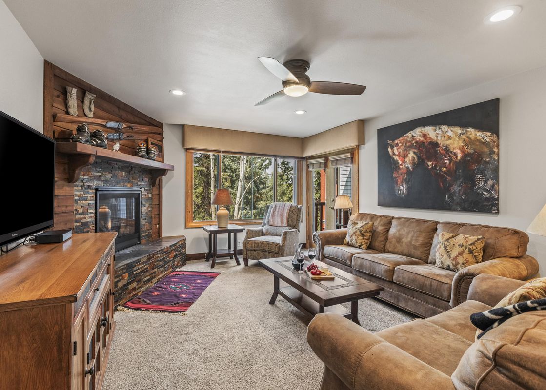 The living room at Snow Flower 56 Park City features comfortable seating, a stone fireplace, and large windows with beautiful outdoor views.