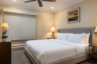 A cozy bedroom with a king-sized bed, white linens, and a unique antler-based lamp on a dark wood nightstand.