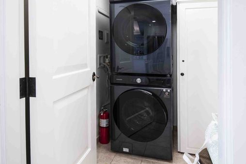 A stacked black washer and dryer unit is visible in a white-doored closet with a red fire extinguisher mounted on the wall.