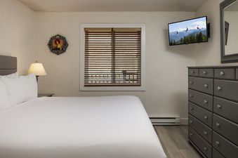 A cozy bedroom at Vantage Point 501 features a king-size bed with white linens, a bedside lamp, a dresser, and a wall-mounted TV.