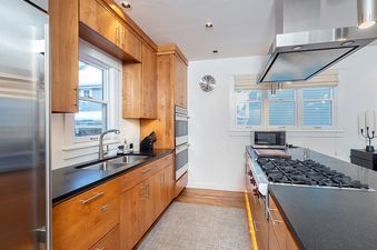 A kitchen with wooden cabinets, black countertops, and stainless steel appliances, including a refrigerator, oven, and stovetop.
