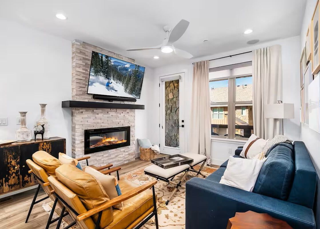 Modern cozy living room at Stage Coach featuring a blue sofa, leather armchairs, and a stone-clad fireplace.