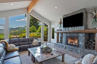A spacious living room at Timer Ridge Retreat features a large stone fireplace, a flat-screen TV, comfortable leather sofas, and expansive windows offering stunning mountain views.