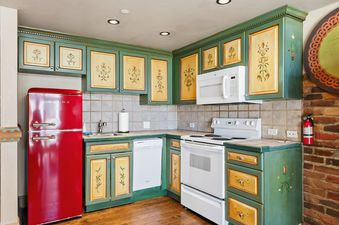 Charming rustic kitchen in Black Forest Dreams with hand-painted green cabinetry and a bold red retro refrigerator.