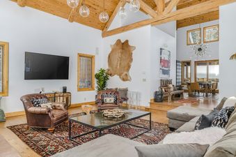 A spacious and inviting living room at Palmyra 94 Mountain Tranquility features vaulted wooden ceilings, a large sectional sofa, leather armchairs, and a flat-screen TV, with a dining area visible in the background.