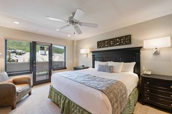 Master bedroom with a king bed, leather armchair, and private balcony door at St James Place 121.