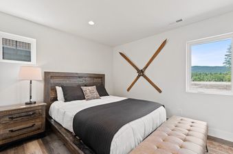 A king bedroom at Quarry A40 features a rustic wooden bed frame, matching nightstand with a lamp, a white comforter with a dark gray throw, decorative pillows, a padded bench, and a unique wall decoration of vintage skis.