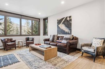 A cozy living room in Highlands Lodge 205 with leather furniture, a light wood coffee table, and a large window revealing a snowy mountain view.