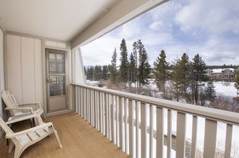 The private balcony offers a serene outdoor space with two chairs and a winter view of snow-covered evergreens and distant mountains.