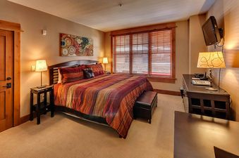 A bedroom with a king-sized bed, a large window, and a flat-screen TV.