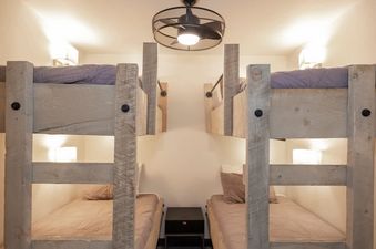 A cozy bunk bedroom at Bullseye Retreat featuring two sets of sturdy wooden bunk beds with comfortable bedding, subtle lighting, and a modern ceiling fan.