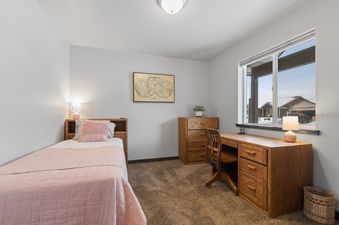 A cozy twin bedroom at Destiny Cove with a pink-quilted bed, a wooden desk and dresser, and a large window providing an exterior view.