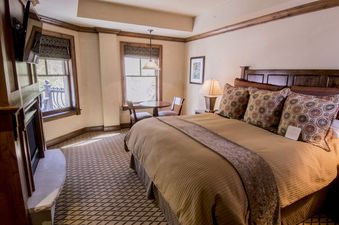 A cozy bedroom in Hyatt 4 Bedroom with a large bed, a fireplace, and a small dining table next to two windows.