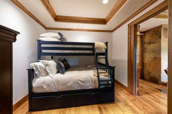 A cozy bunk room at Chateau Beaver Creek Residence 210 with a black bunk bed, white bedding, and wooden accents on the ceiling and trim.