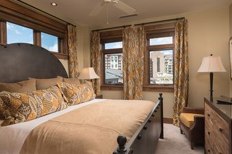 A cozy bedroom with a large bed, patterned curtains, and a television, offering a view of the city outside.