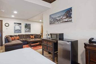 A comfortable living area in The Charter E345 with a brown sectional sofa, a rustic wooden coffee table, and a mini-kitchen area featuring a microwave and a small refrigerator.