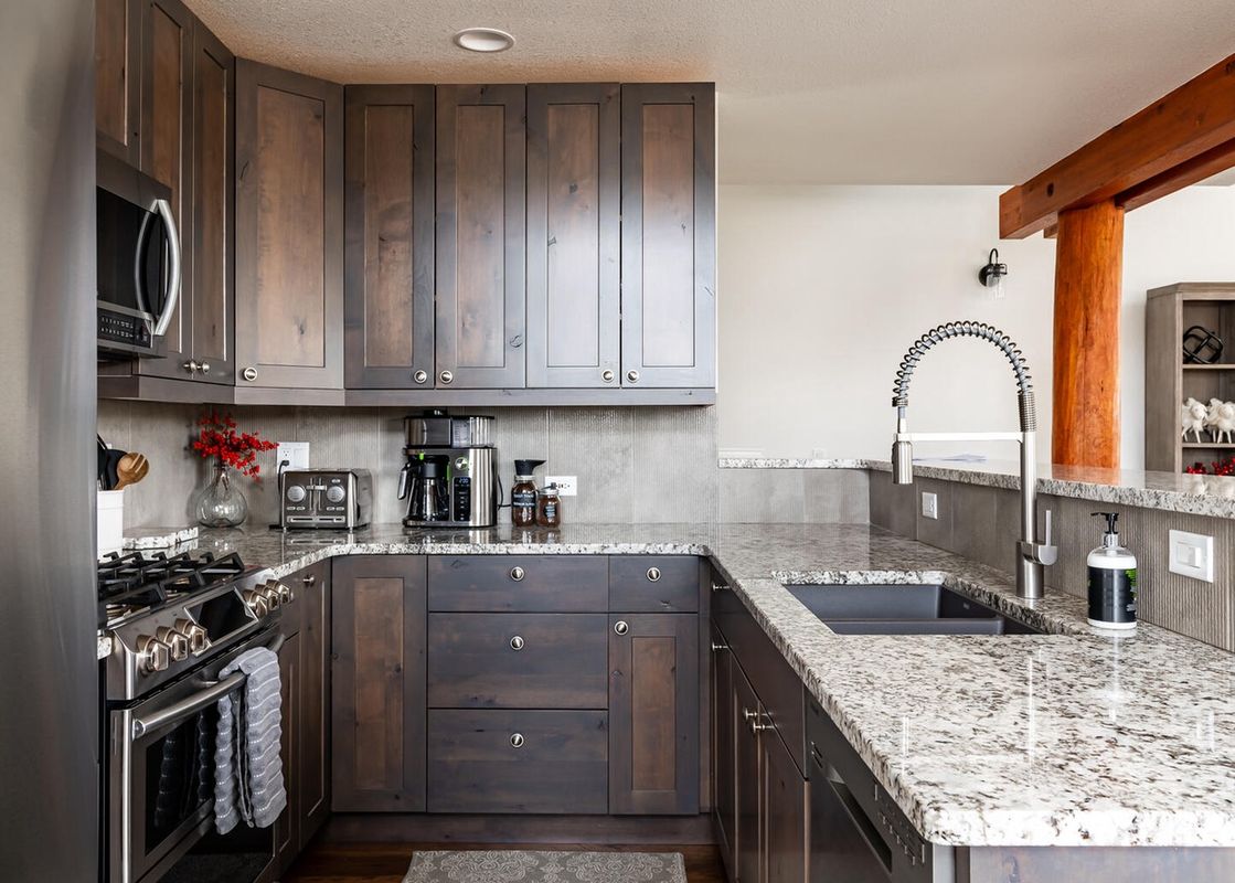 The kitchen of Moonlight Basin Saddle Ridge D1 features a granite countertop, stainless steel appliances, and dark wood cabinets.