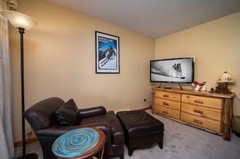 The comfortable sitting area at Silverado I C101 features a leather armchair, a footstool, a TV on a rustic wooden dresser, and a floor lamp, creating a cozy and inviting atmosphere.